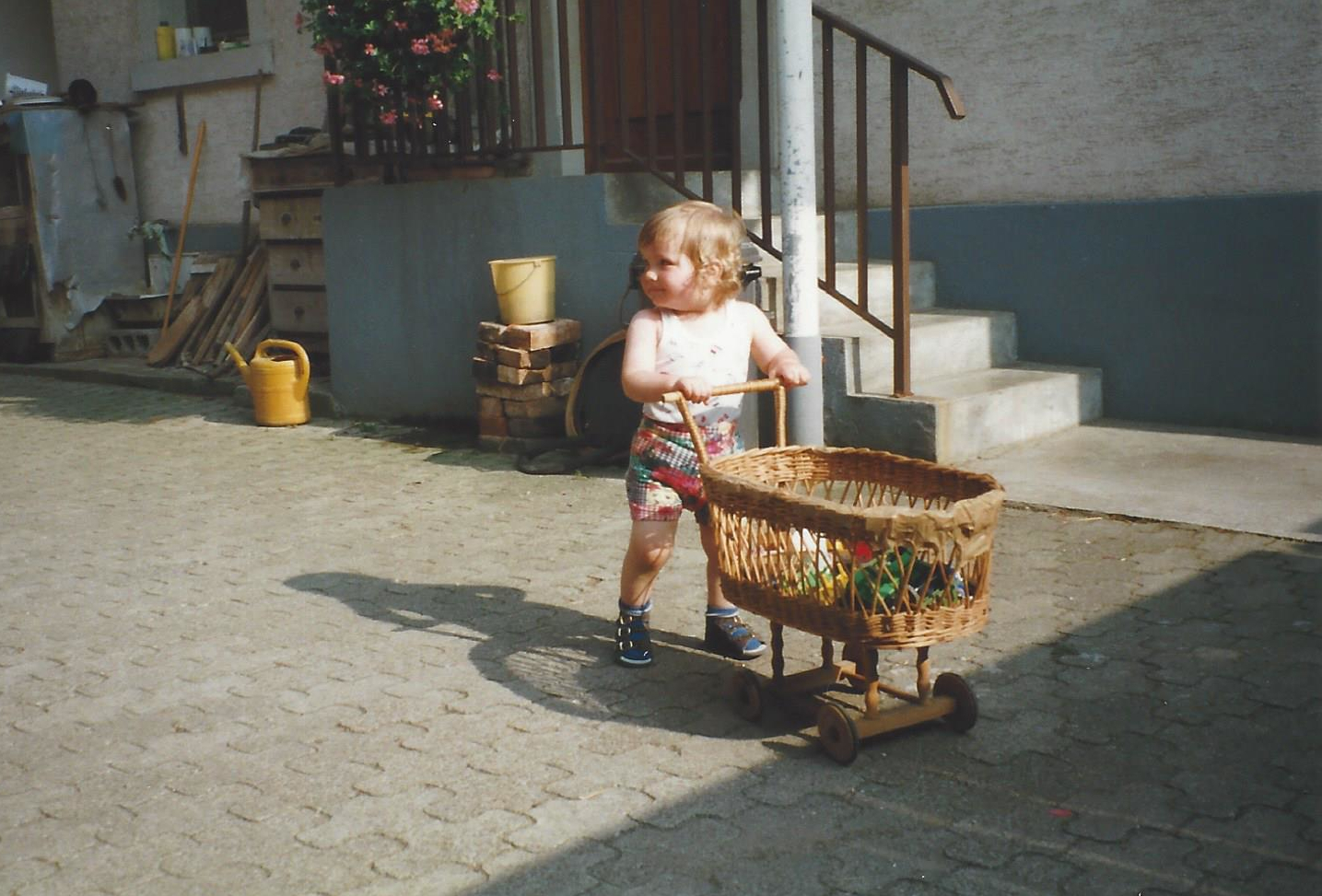 Laura schiebt als Kleinkind laufend einen Puppenwagen. Das ganze geschieht offensichtlich auf einem alten Bauernhof. Es sind drumherum Gieskannen, Gartengeräte und anderes Bauernhof-Zubehör zu sehen.