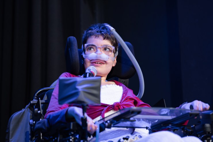 Laura in einer Portraitaufnahme. Hintergrund ist blau beleuchtet. Ein Mikrofon ist vor ihr.